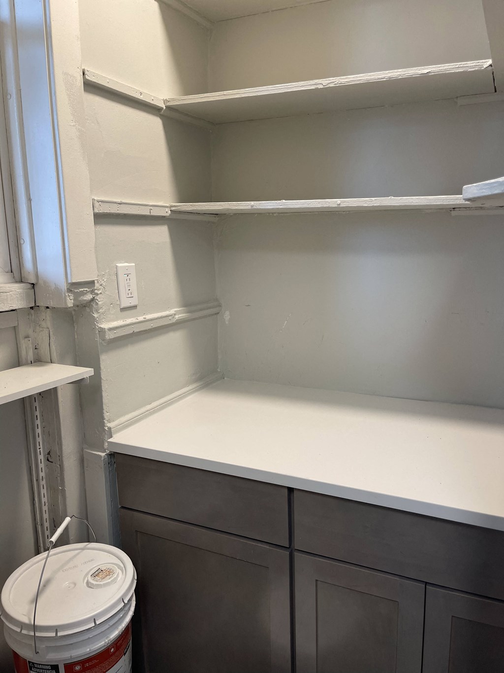 an empty shelf in a kitchen with a trash can