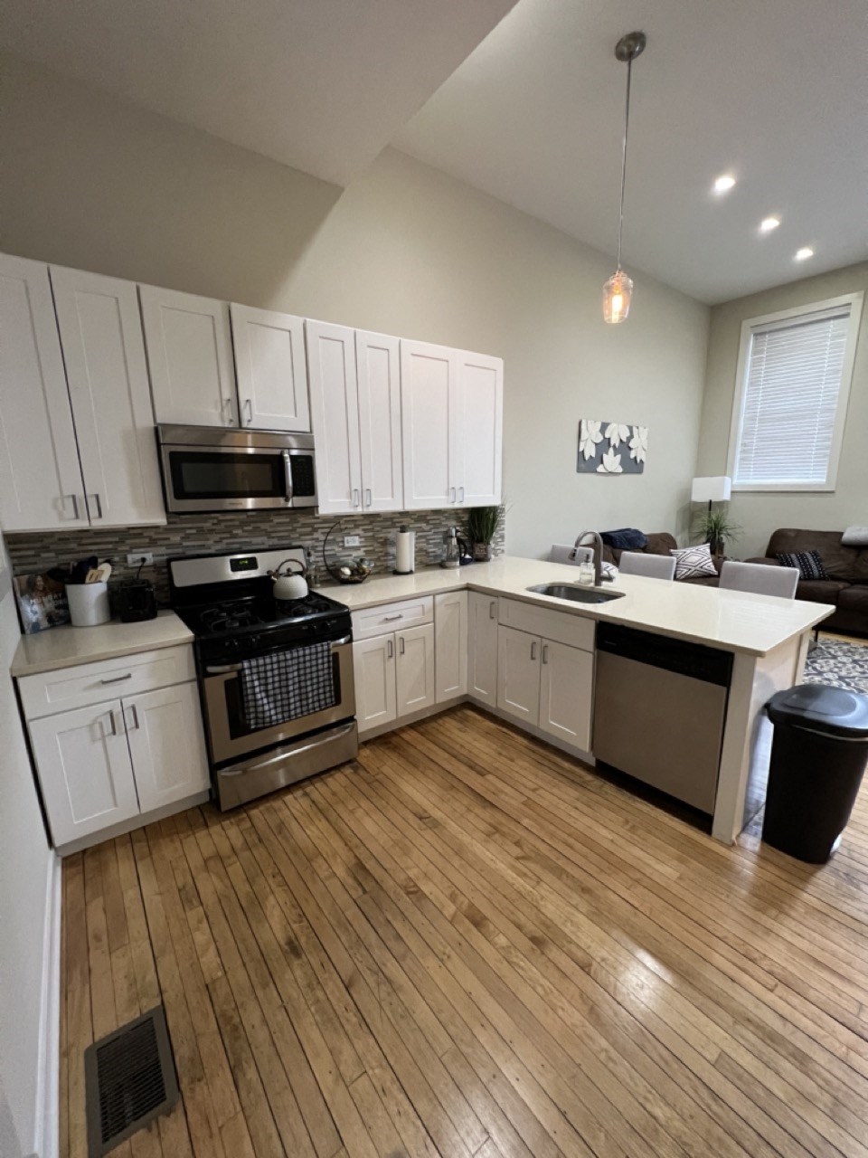 a kitchen and living room with white cabinets and a wooden floor