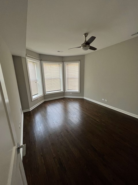 an empty room with a ceiling fan and three windows