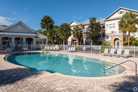 A large swimming pool surrounded by a brick patio and lounge chairs.