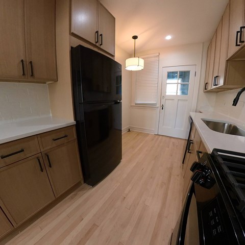 A kitchen with a black fridge and wooden cabinets.