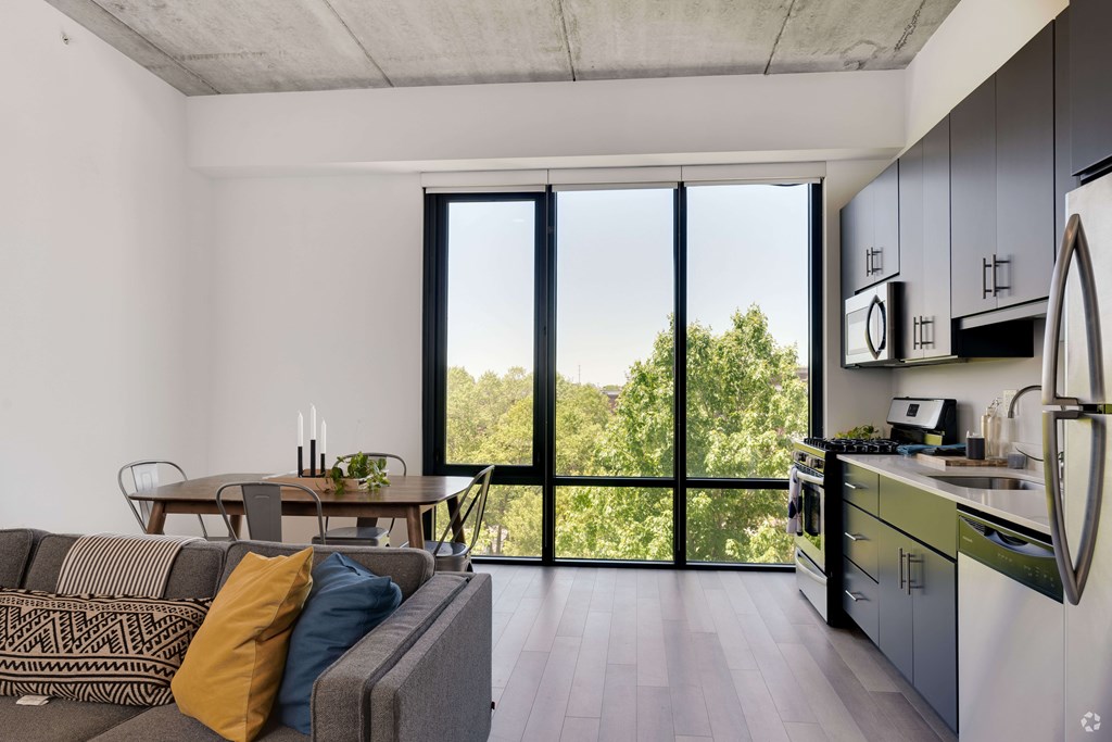 A modern kitchen with a dining table and a couch with a view of trees outside.