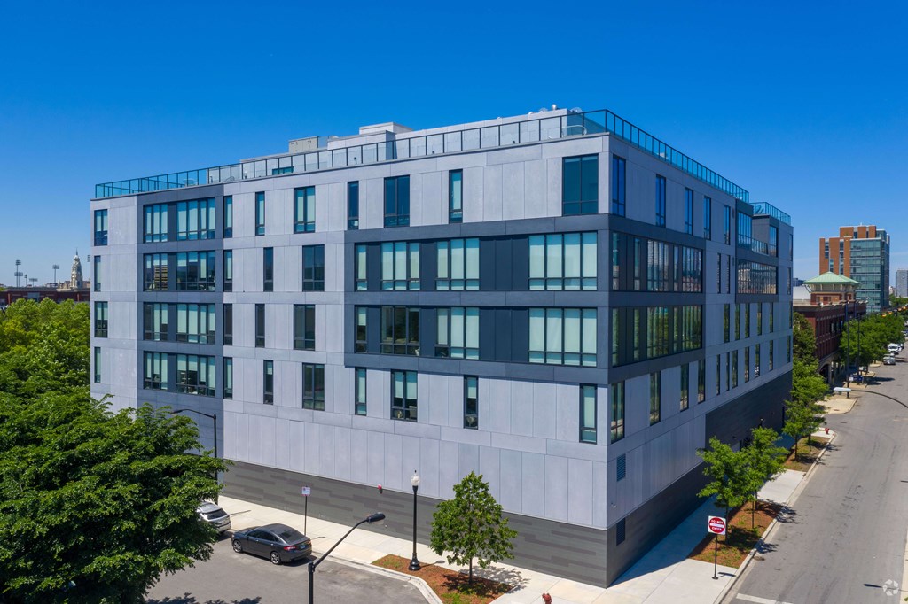 A modern building with a flat roof and large windows is surrounded by a sidewalk and street.