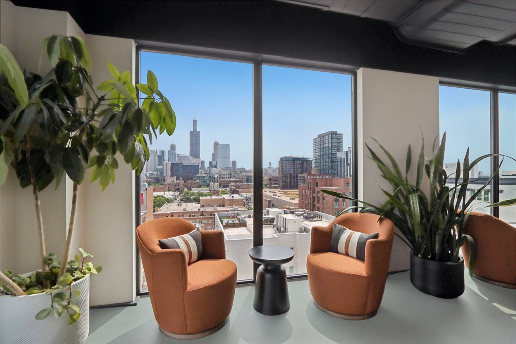 A room with orange chairs and plants with a view of the city.