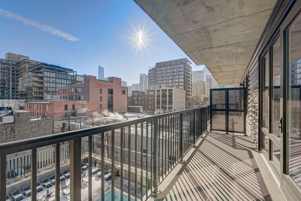 A balcony with a metal railing overlooks a parking lot and buildings.