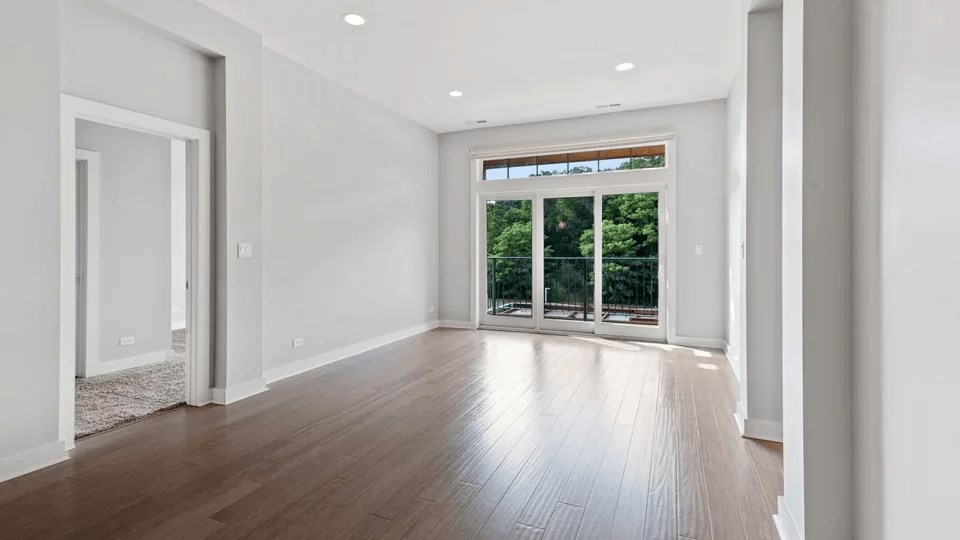 A room with a wooden floor and a sliding glass door leading to a garden.