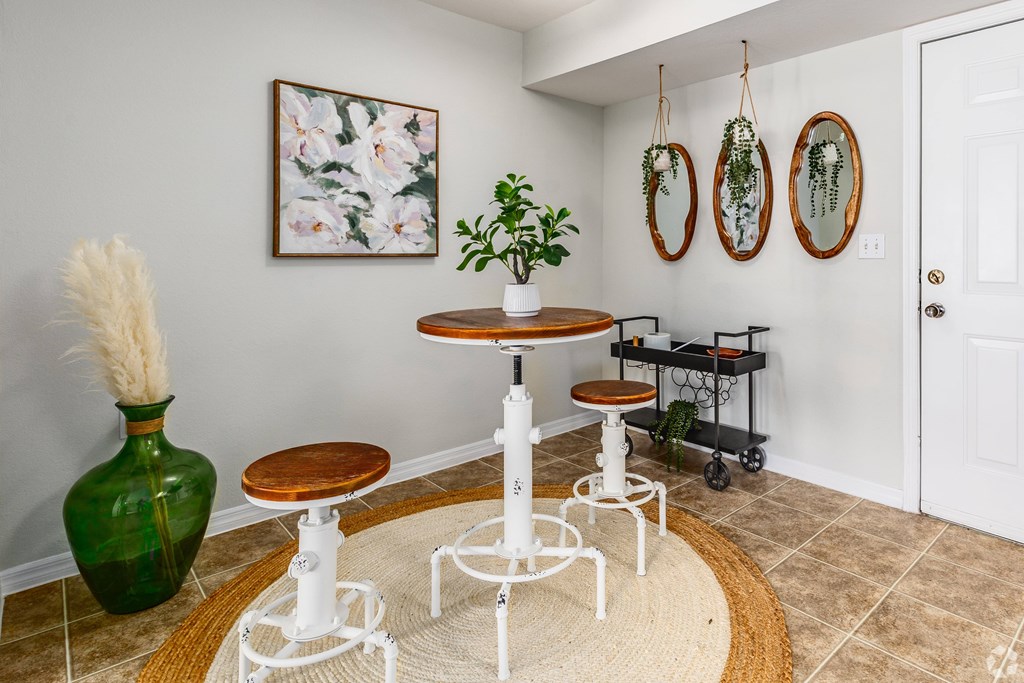 A green vase sits on a white table in a room with a white wall and a painting hanging on it.