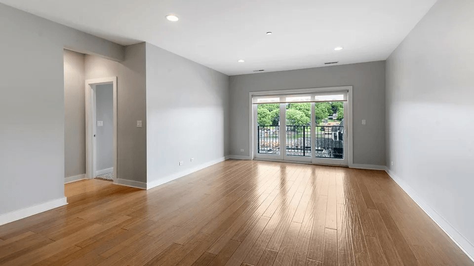 A room with wooden floors and a sliding glass door leading to a balcony.