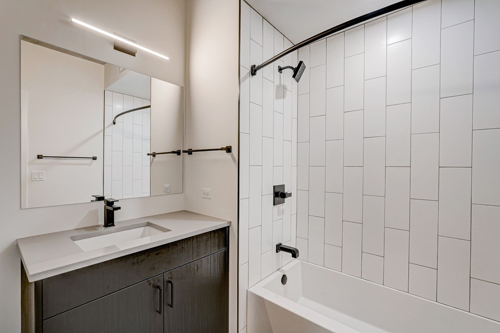 A white tiled bathroom with a sink and a bathtub.