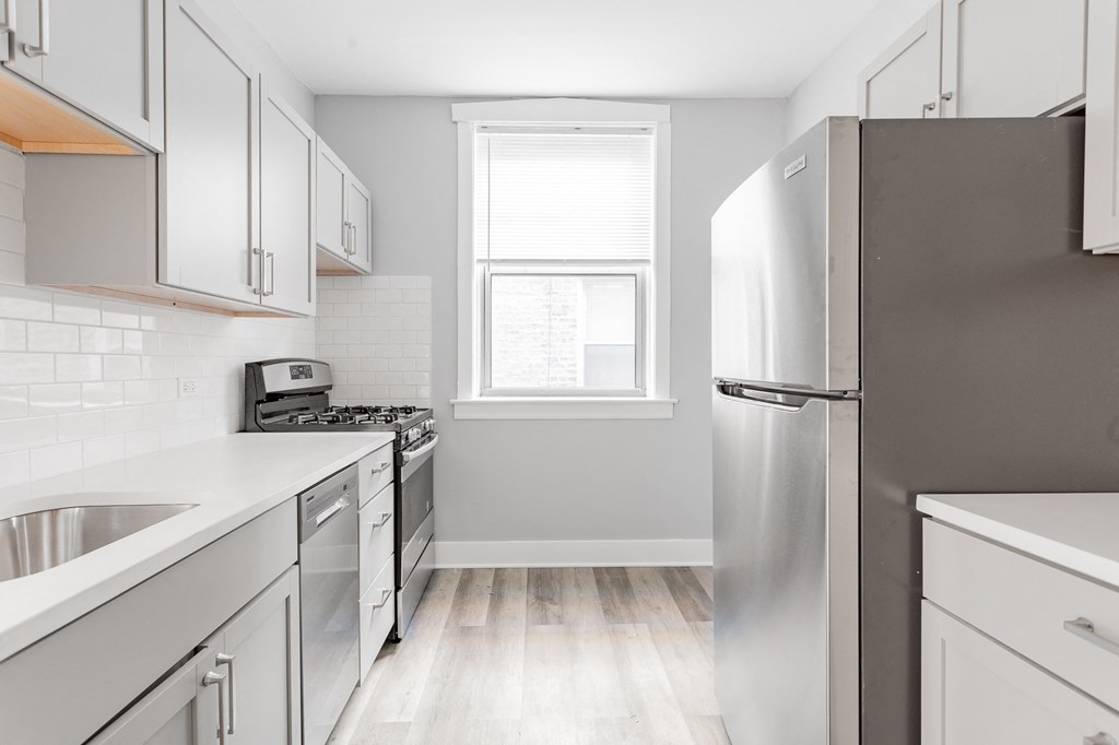an all white kitchen with stainless steel appliances and a window