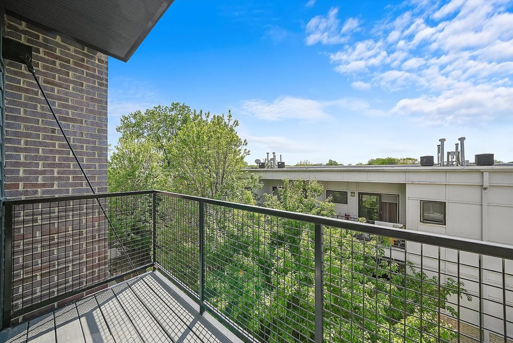 A balcony with a black railing overlooks a green yard and a building.