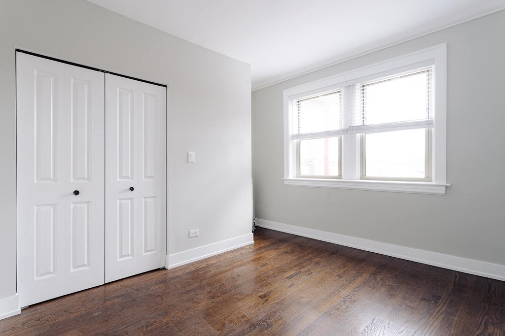 a bedroom with white walls and wood floors and a window