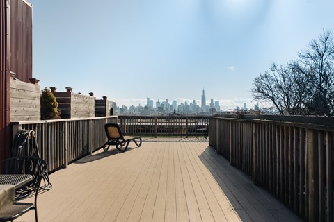 A wooden deck with a chair and a table overlooking a city skyline.