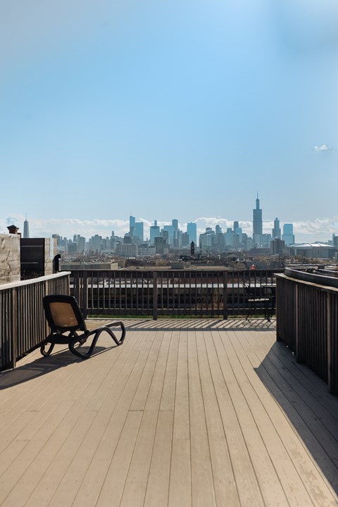 A chair is on a wooden deck with a city skyline in the background.