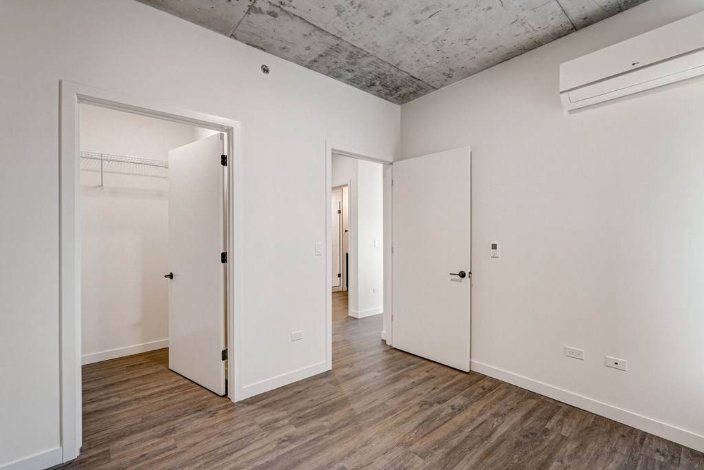 A room with white walls and wooden floors has two open doors.