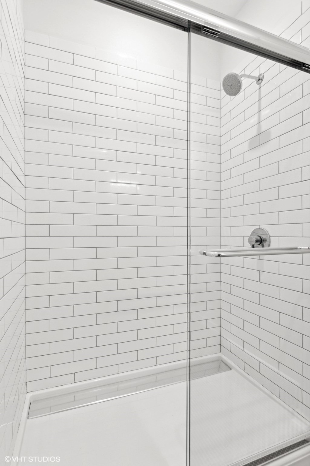 A white tiled shower with a glass door.