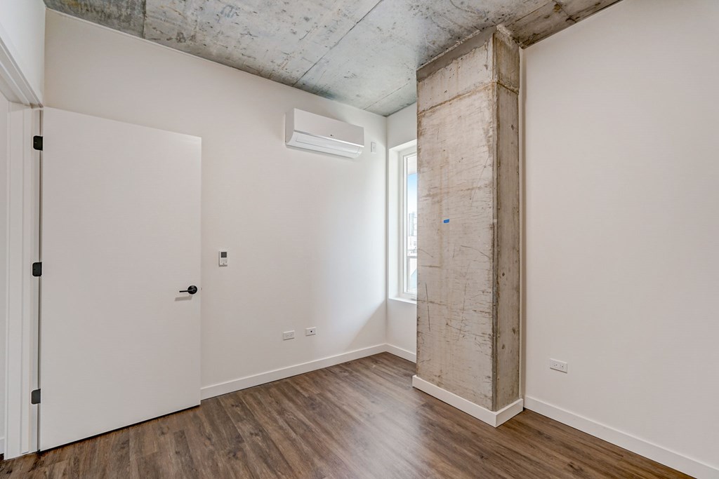 A room with a white door and a window with a concrete wall on the right side.