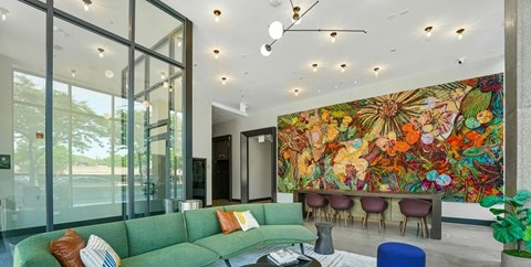 A living room with a green couch and a large mural on the wall.