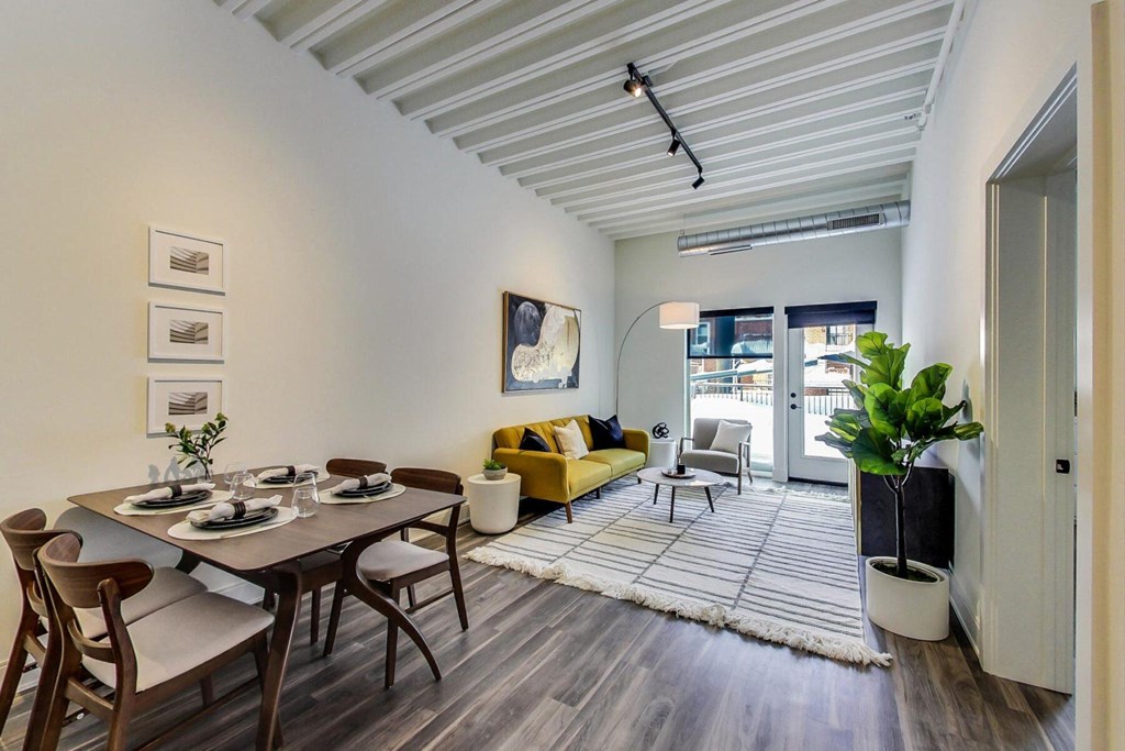 a living area with a wooden table and chairs, a yellow couch and a sliding glass door