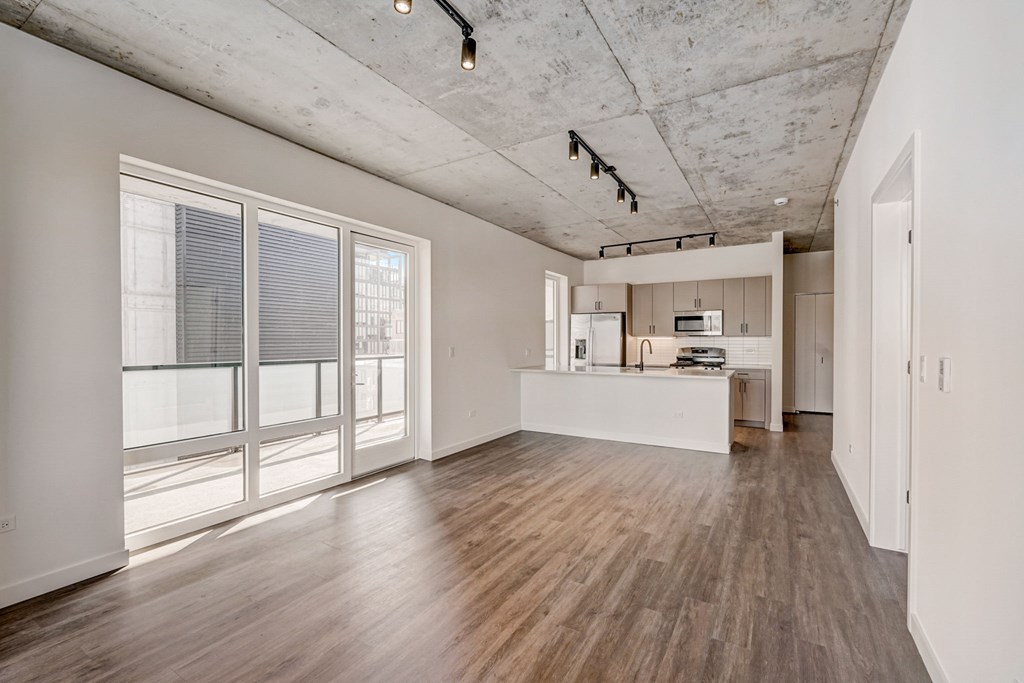 A spacious room with wooden floors and a kitchen area in the background.