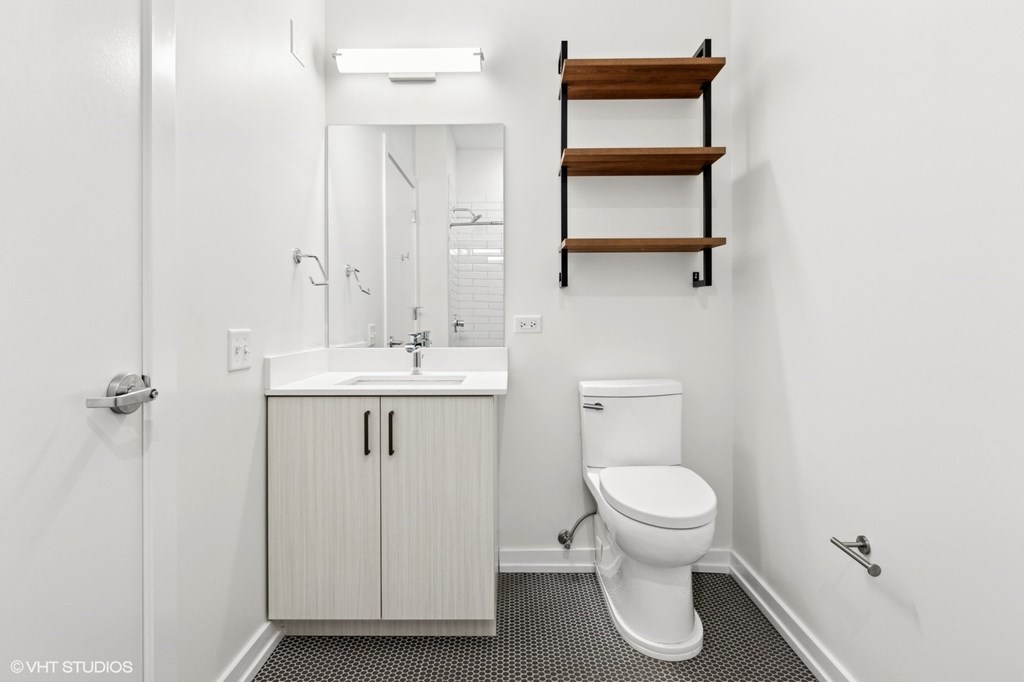 A white toilet sits under a shelf in a bathroom.