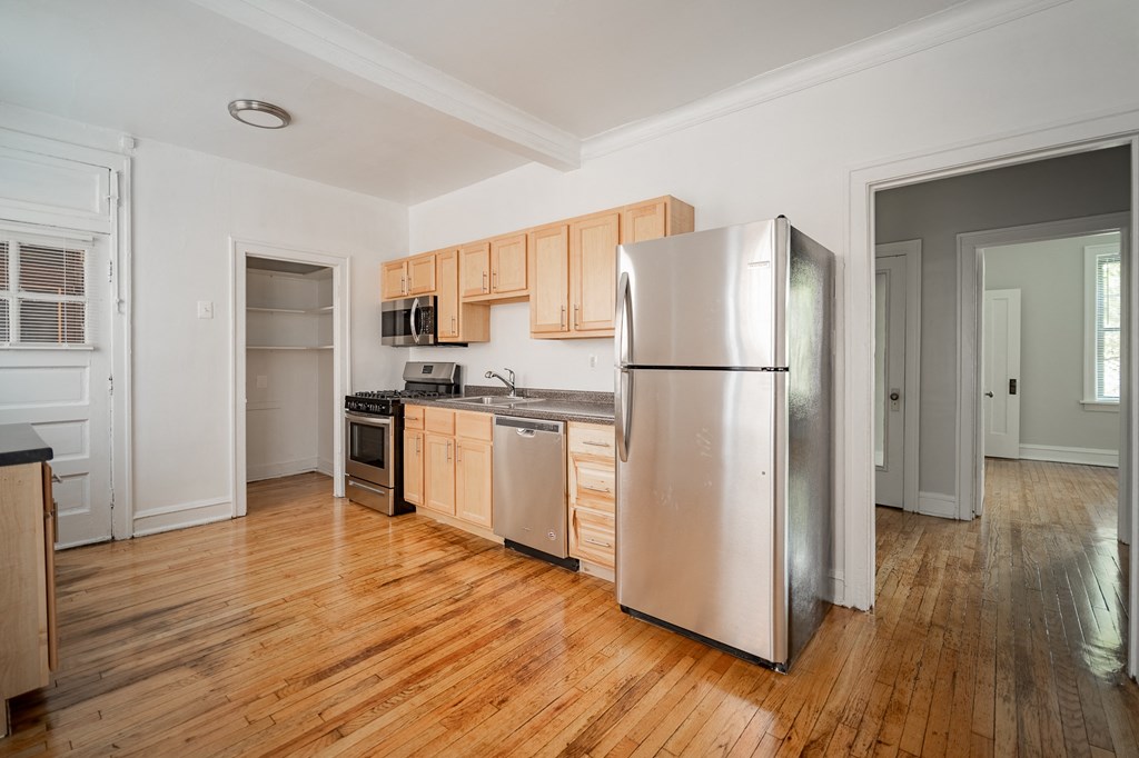 an empty kitchen with stainless steel appliances and wooden floors