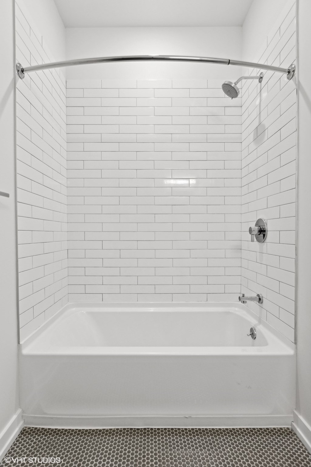 A white tiled bathroom with a white tub and shower.