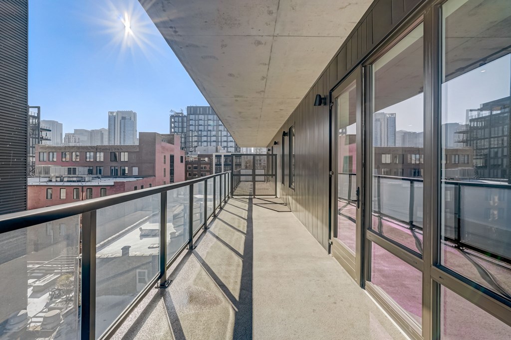 A long balcony with glass doors and windows overlooking a cityscape.