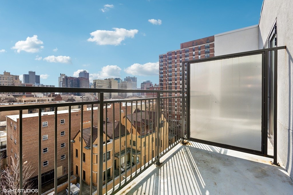 A balcony with a metal railing and a glass door overlooks a cityscape.