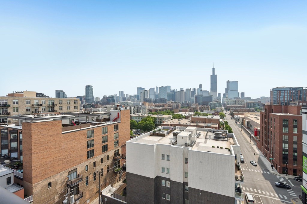 A cityscape with a mix of modern and older buildings, a clear sky, and a busy street with cars.