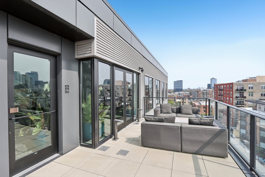 A modern balcony with a grey couch and glass doors.