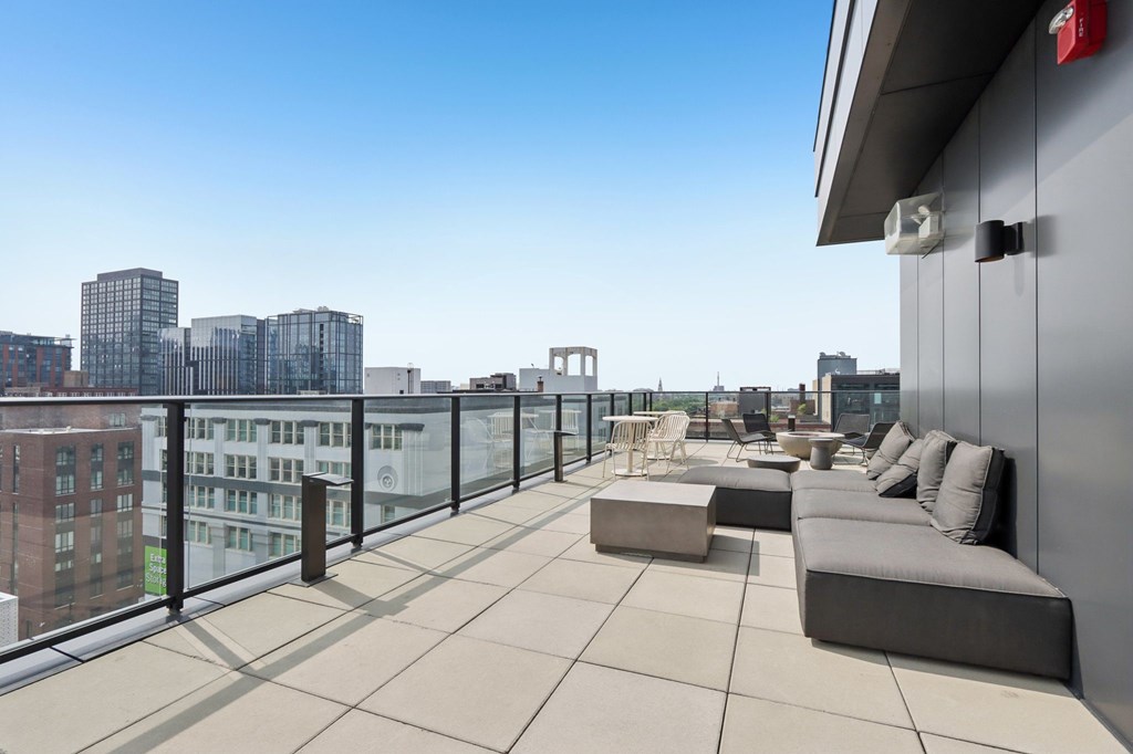 A balcony with a couch, table, and chairs overlooking a cityscape.