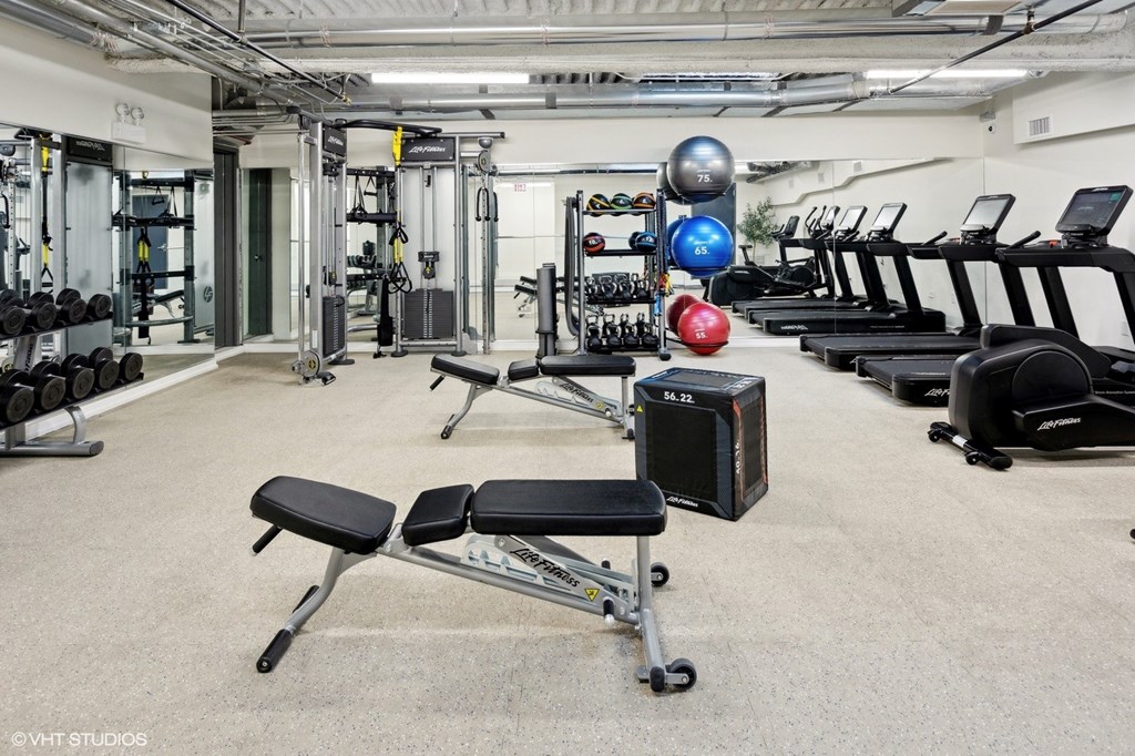 A gym with a variety of equipment including treadmills, weights, and exercise balls.
