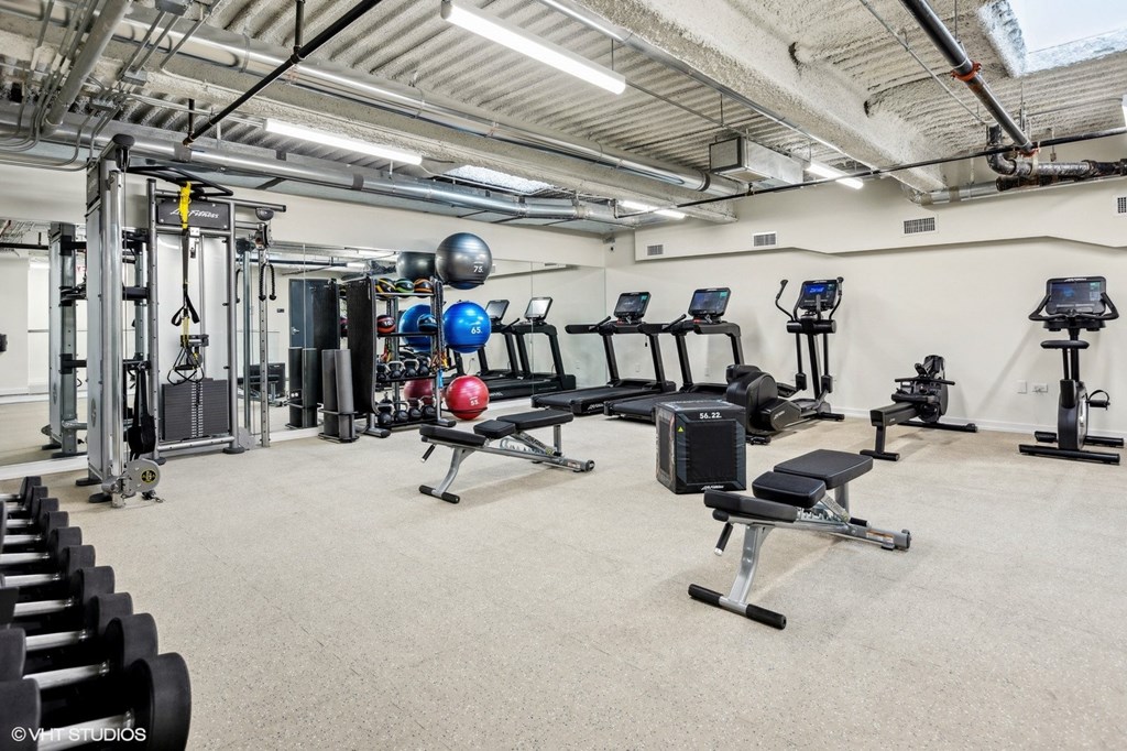 A spacious gym with various exercise equipment and a grey carpeted floor.