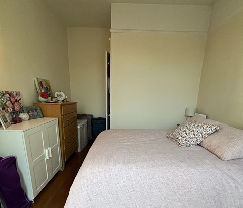 A bedroom with a bed, nightstand, and a dresser with a clock and picture frame on top.
