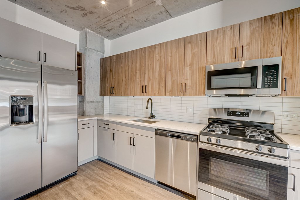 A kitchen with a stainless steel refrigerator, a stainless steel dishwasher, a stainless steel oven, and wooden cabinets.