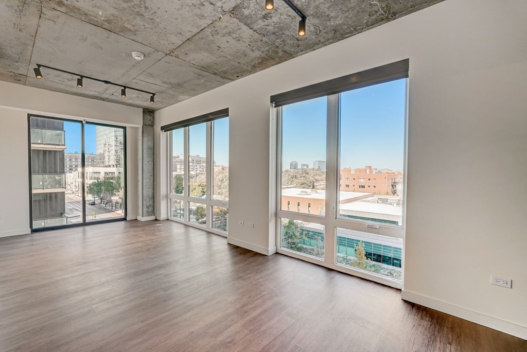A large empty room with wooden floors and a view of the city through the windows.