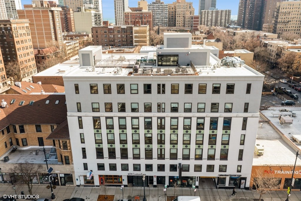 A white building with a black roof is surrounded by other buildings.