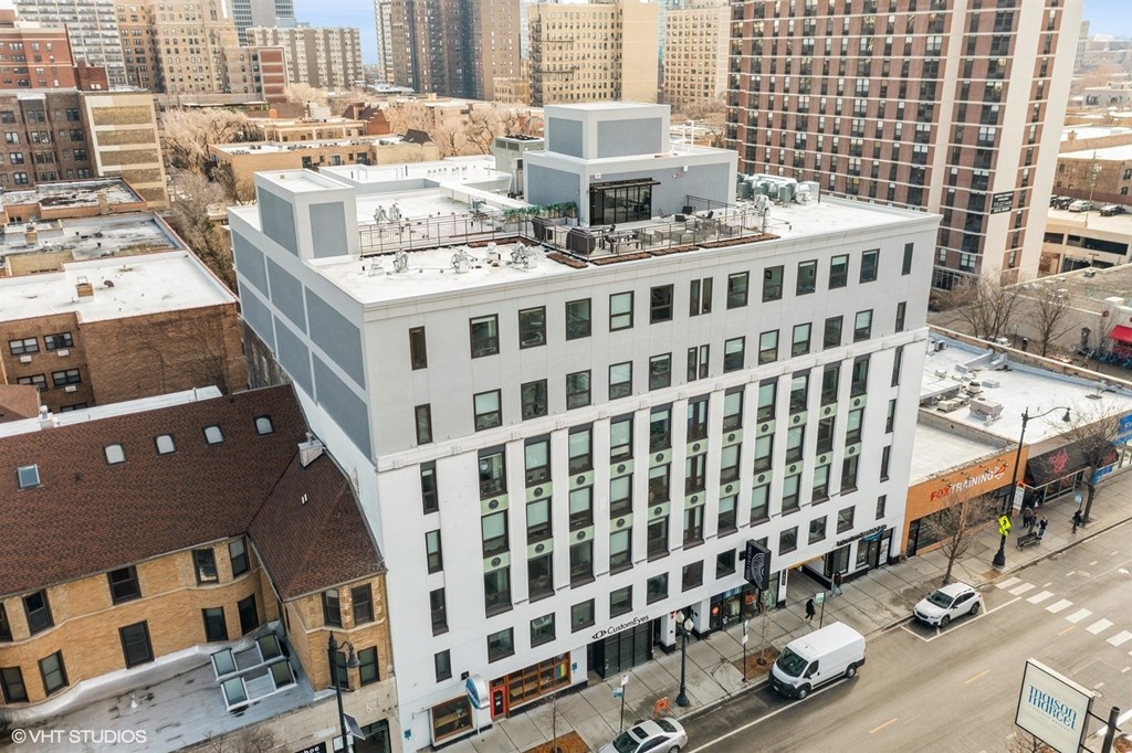 A modern white building with a flat roof is surrounded by other buildings.