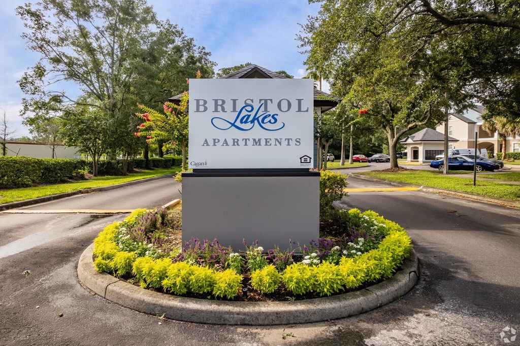 A sign for Bristol Lakes Apartments is surrounded by flowers and greenery.