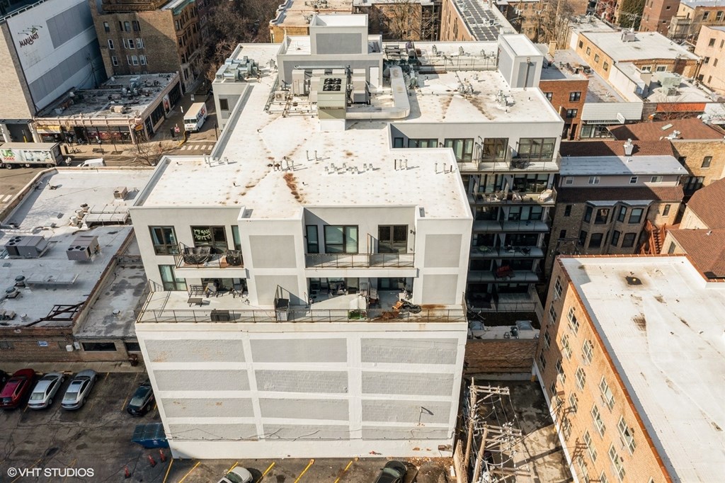 A large white building with a flat roof is surrounded by other buildings.