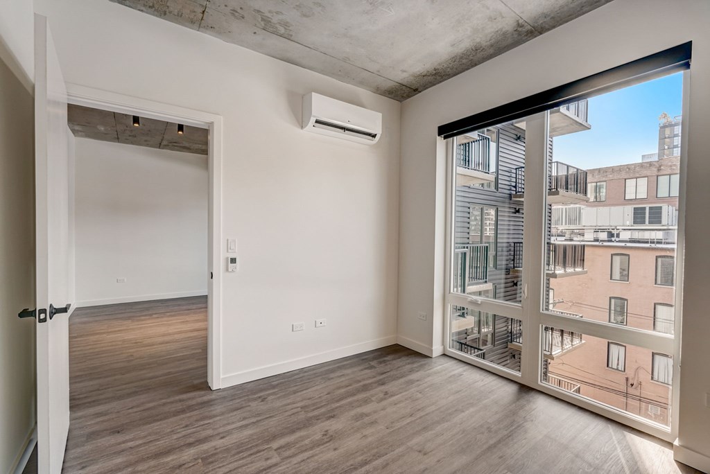 A room with a sliding glass door leading to a balcony with a view of a cityscape.