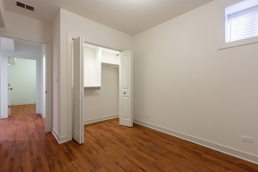A room with white walls and wood flooring with a doorway open to another room.
