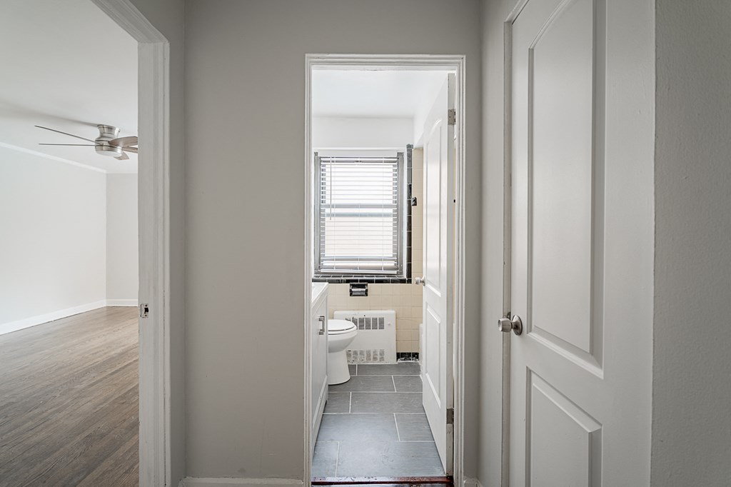 A hallway with a door on the right and a window with blinds on the left.