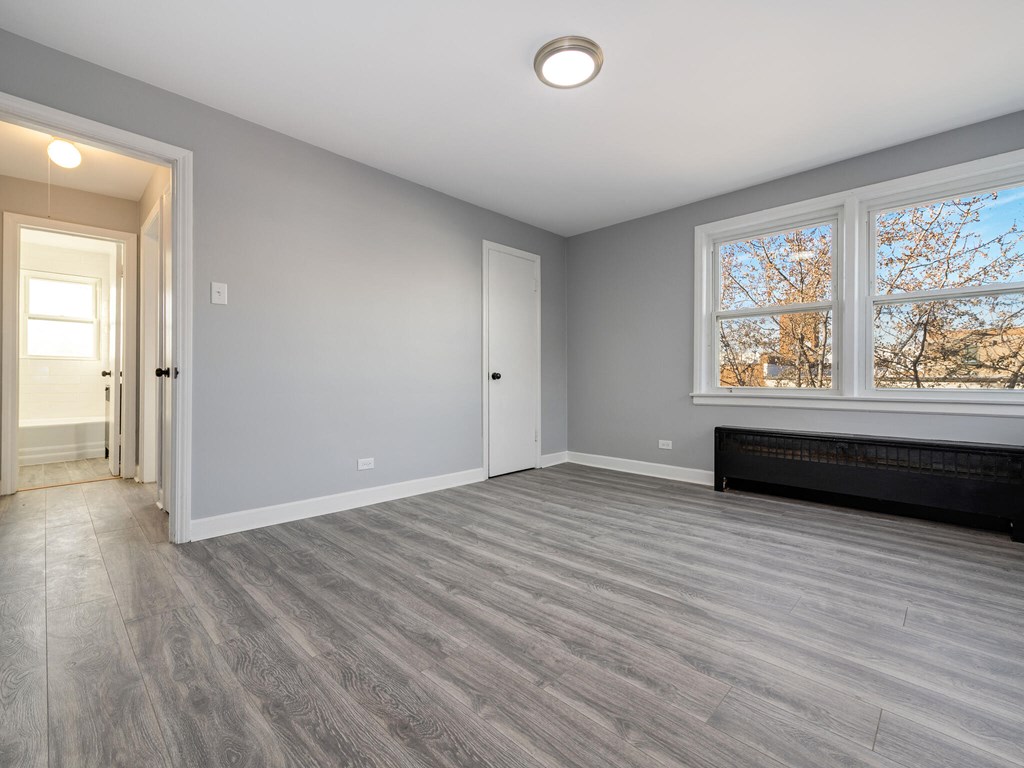 A room with a grey floor and a window with a view of a tree and a building outside.