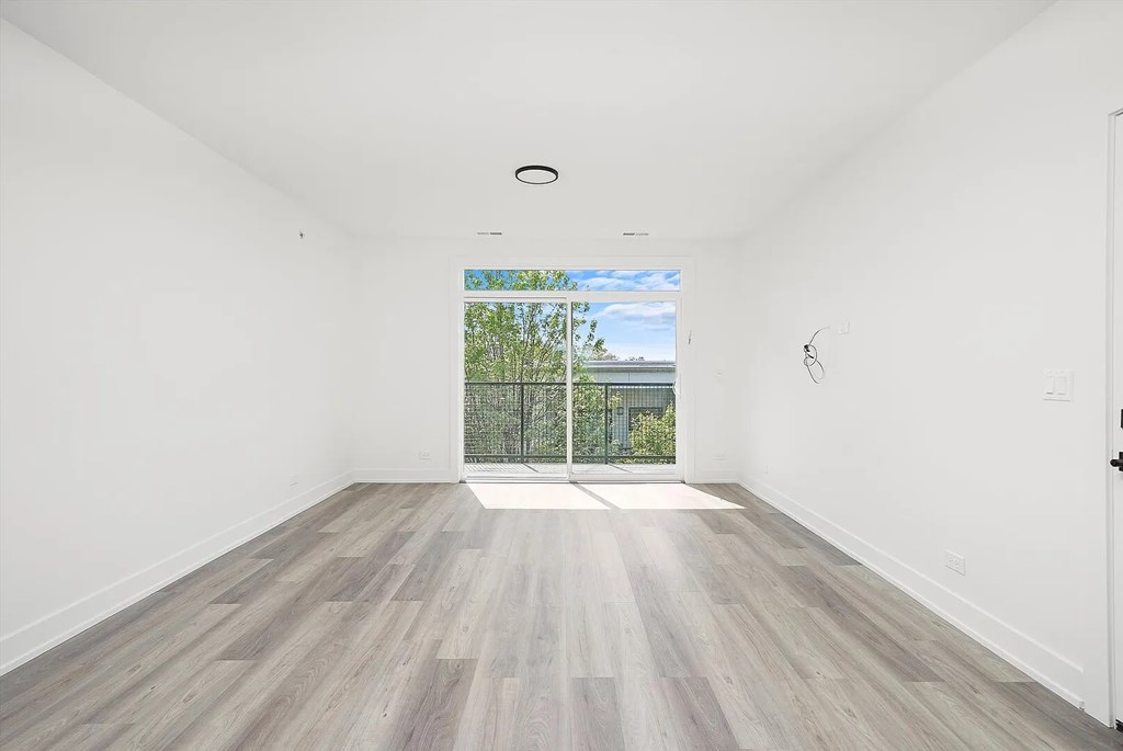 A room with a wooden floor and a view of a fence and trees outside.
