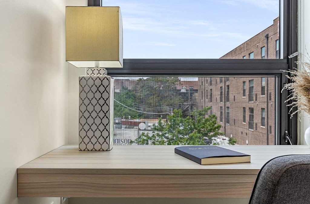 a desk with a book and a lamp in front of a window
