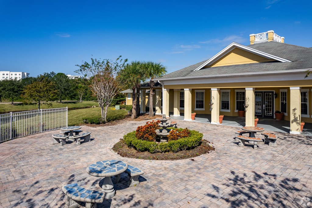 A building with a yellow roof and columns is surrounded by a circular garden with a bench.