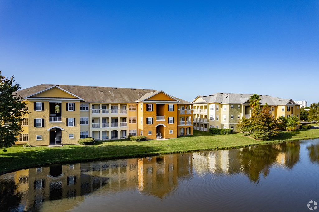 A large building with a yellow facade is reflected in the water in front of it.