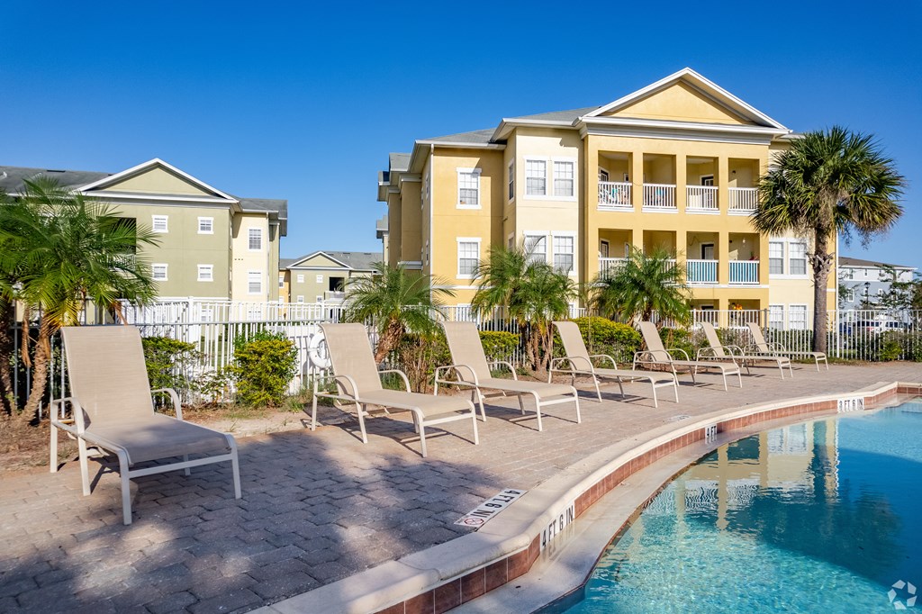 A pool area with chairs and a building in the background.